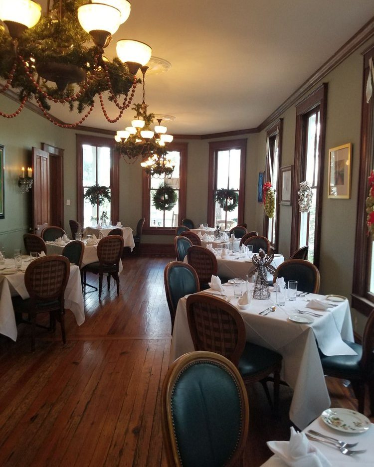 A dining room at The Sycamore House with chandeliers, hardwood floors and white-linen tables