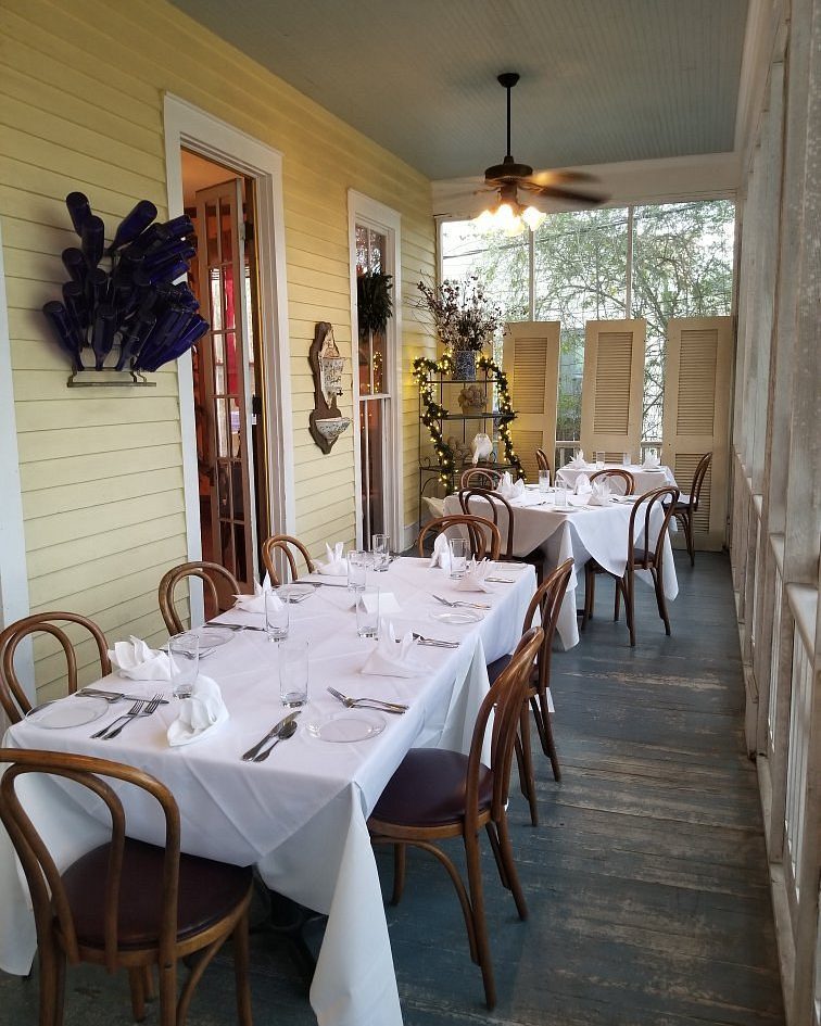 Tables set with white linens and cane chairs on the screened porch at The Sycamore House